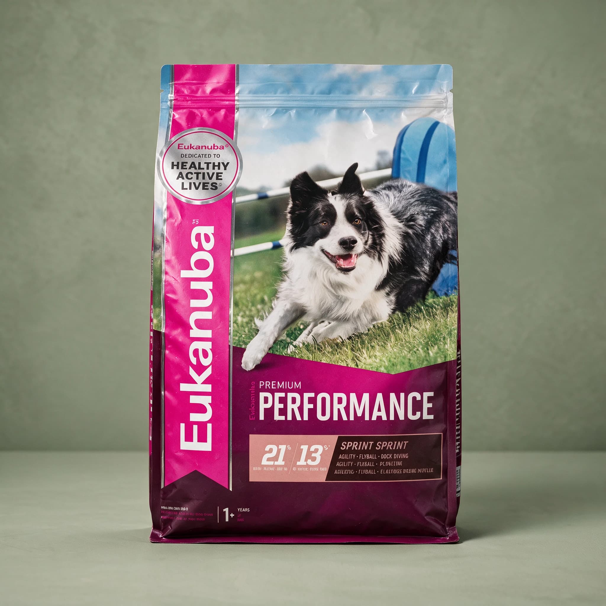 The pink and dark purple Eukanuba Premium Performance 21/13 "Sprint" dry dog food bag with "Agility, Flyball, Dock Diving" text, featuring a black-and-white Border Collie running through an agility course on grass, photographed against a sage green studio background.