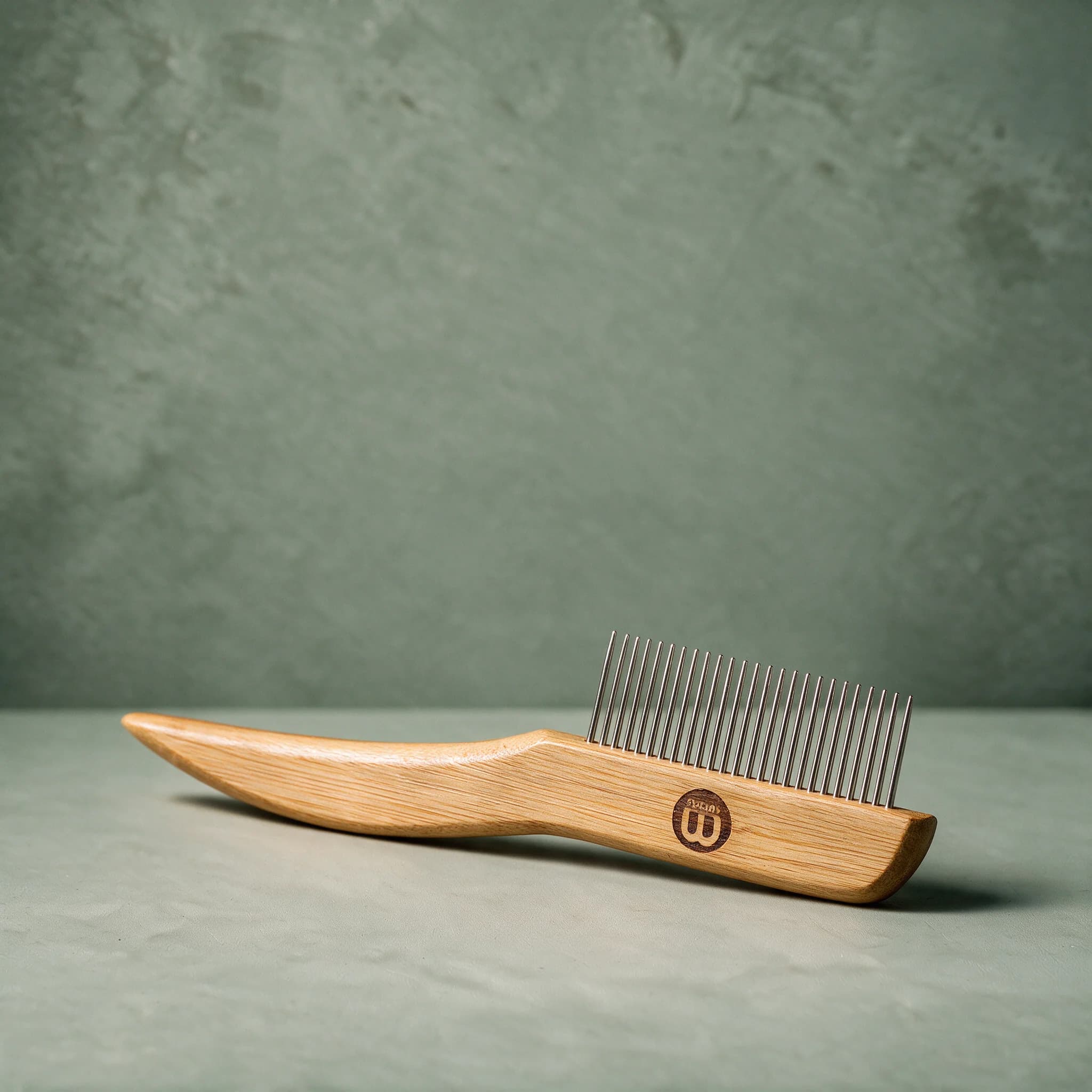 Mikki Bamboo Anti-Tangle Comb with a bamboo handle and a row of long, rounded stainless steel teeth, shown on a sage green background.