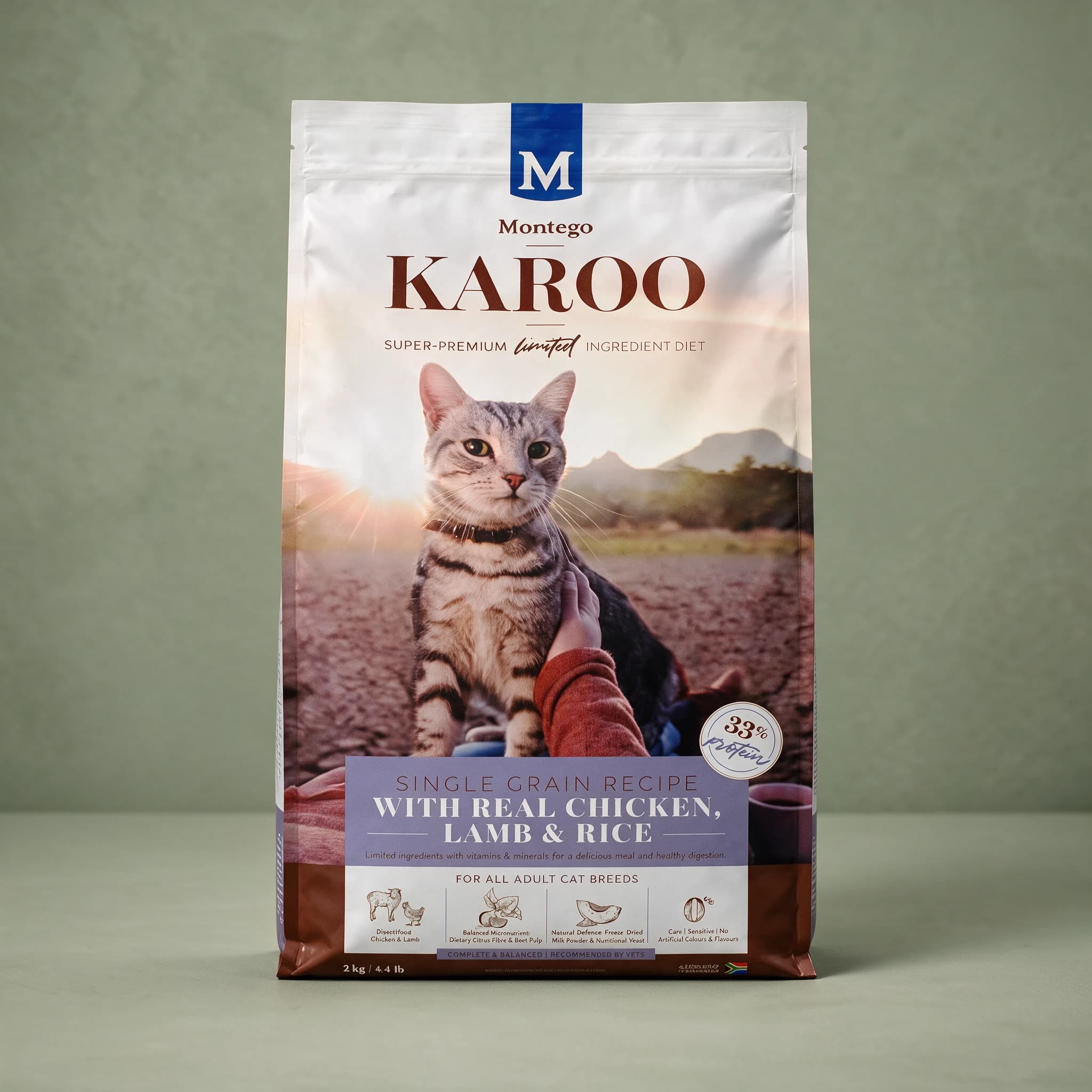 The white Montego Karoo dry cat food bag, showing a photo of a person's hand stroking a grey tabby cat in a Karoo desert sunset landscape, a lavender "SINGLE GRAIN RECIPE WITH REAL CHICKEN, LAMB & RICE" banner, a "33% protein" badge, and "2kg/4.4lb" printed near the base, standing upright against a