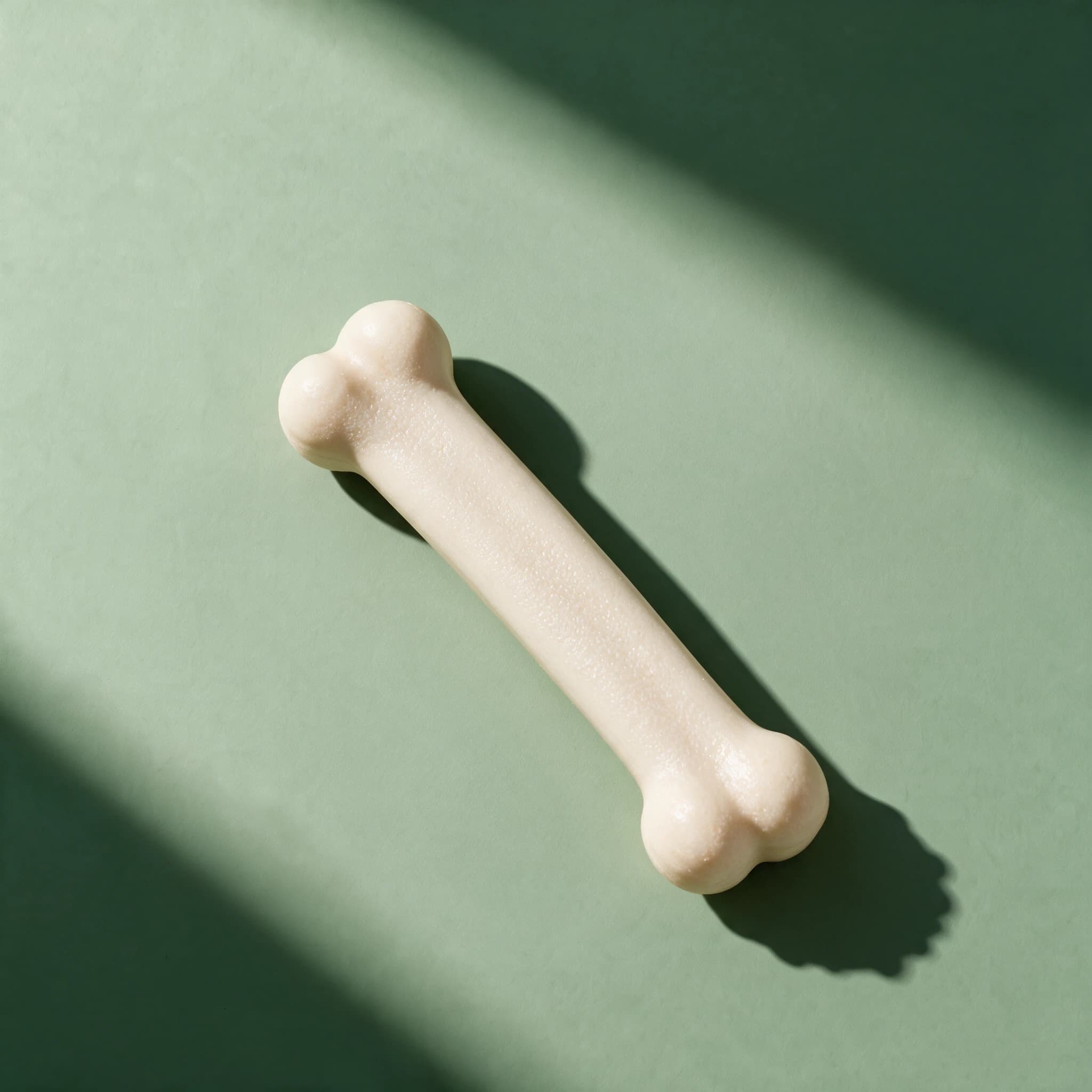 A single cream-colored Nylabone Extreme Bone Chew, a hard textured chew bone with rounded knobbed ends, shown overhead against a sage green background.