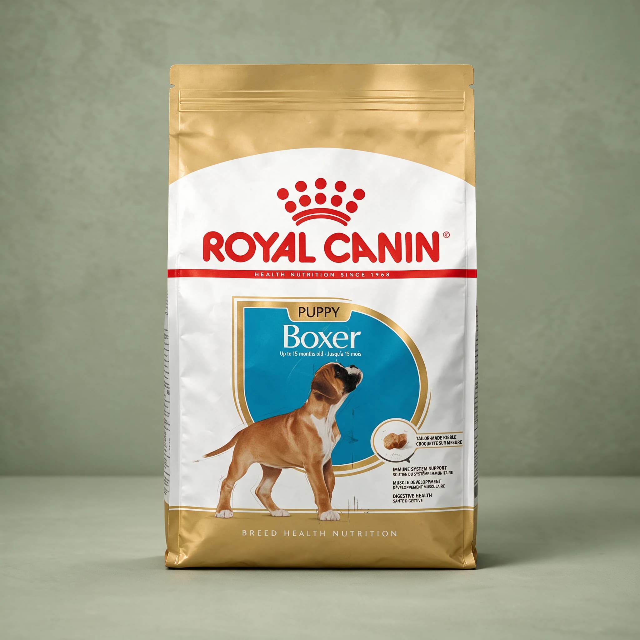 The gold Royal Canin Boxer Puppy dry dog food bag, featuring an illustration of a fawn Boxer puppy and breed-specific nutrition branding, photographed against a plain sage green studio background.
