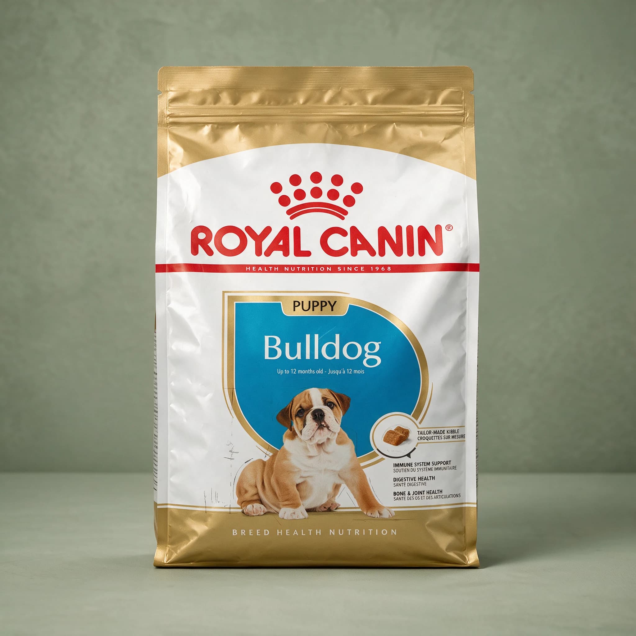 The Royal Canin Bulldog Puppy dry dog food bag with the red crown logo and an illustration of a Bulldog puppy, photographed against a plain sage green studio background.