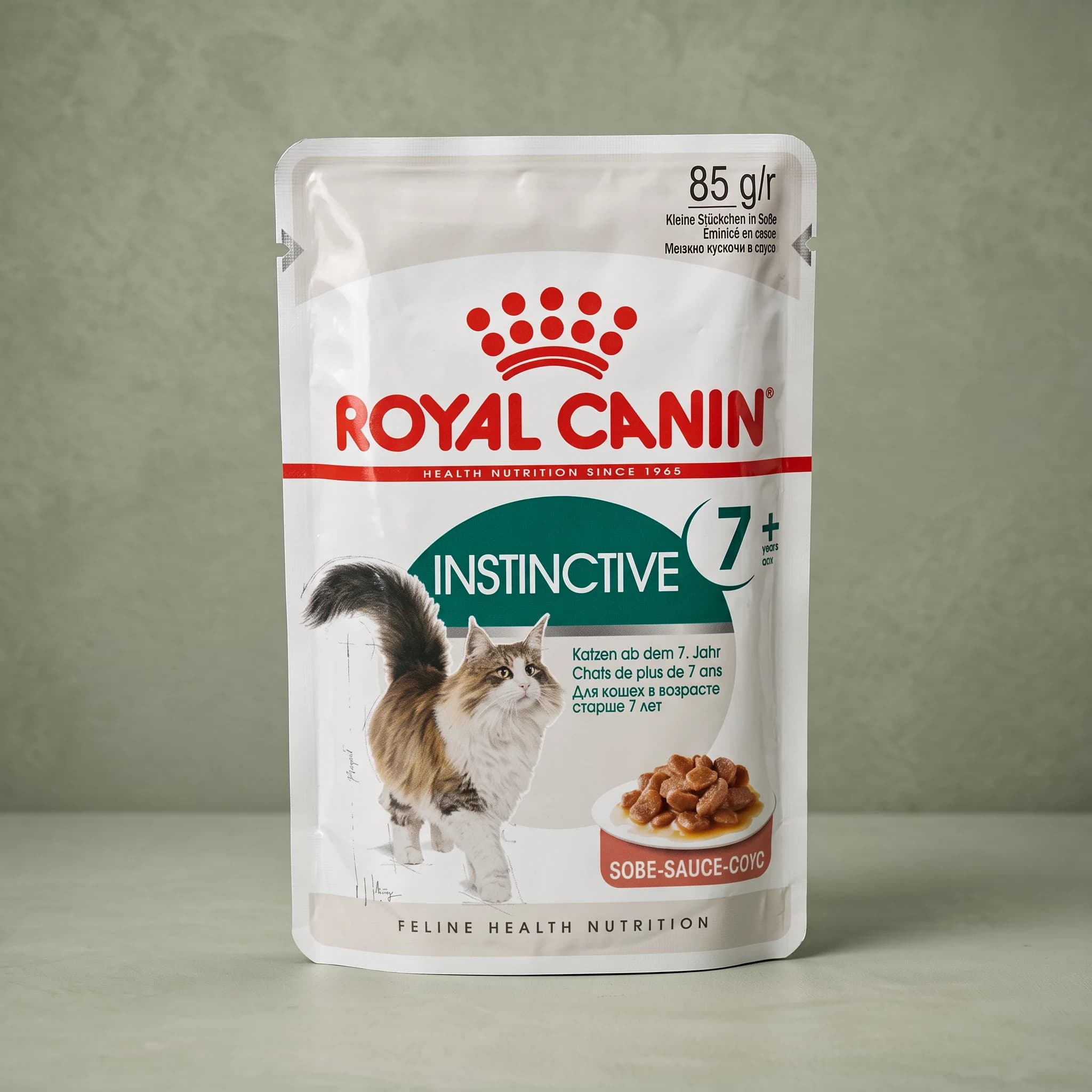 A gold Royal Canin Instinctive Adult 7+ wet cat food pouch showing chunks in gravy on the front label, photographed against a plain sage green studio background.